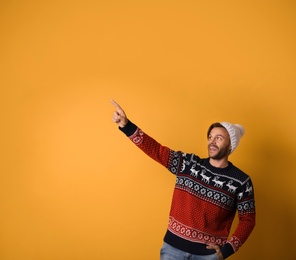 Young man in Christmas sweater and hat on yellow background. Space for text