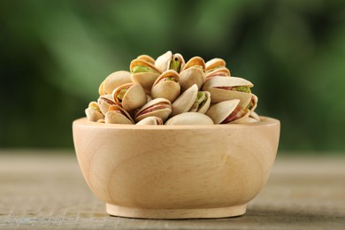 Photo of Tasty pistachios in bowl on wooden table against blurred background, closeup