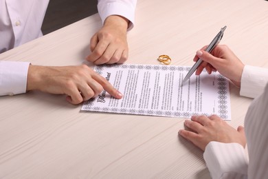 Photo of Man and woman signing marriage contract at light wooden table, closeup