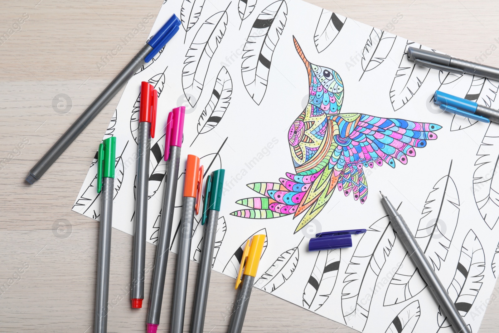 Photo of Antistress coloring page and felt tip pens on light wooden table, flat lay