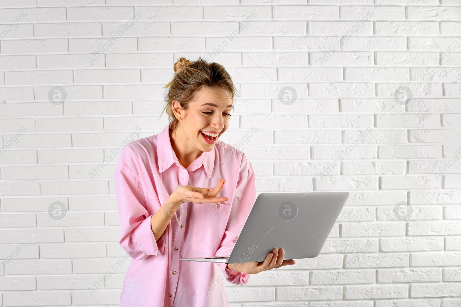Photo of Woman using laptop for video chat against brick wall