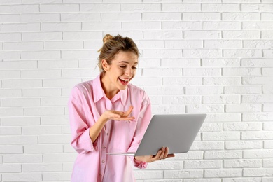 Woman using laptop for video chat against brick wall