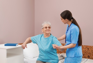 Photo of Nurse assisting senior woman on bed in hospital ward