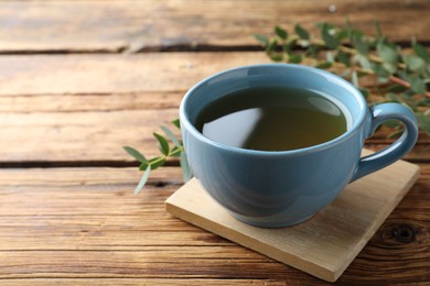 Photo of Cup of green tea and eucalyptus leaves on wooden table. Space for text