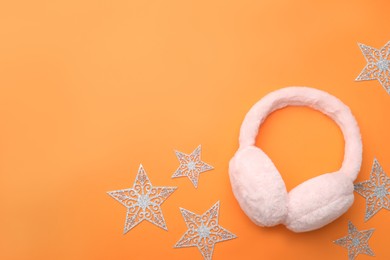 Photo of Stylish winter earmuffs and decorative stars on orange  background, flat lay. Space for text