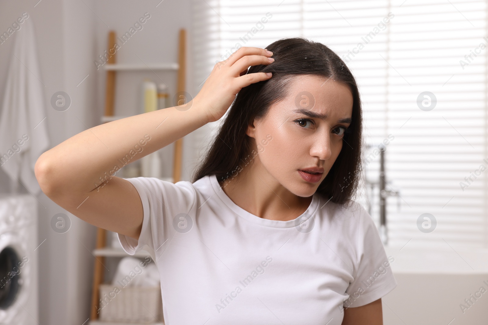 Photo of Emotional woman examining her hair and scalp in bathroom. Dandruff problem