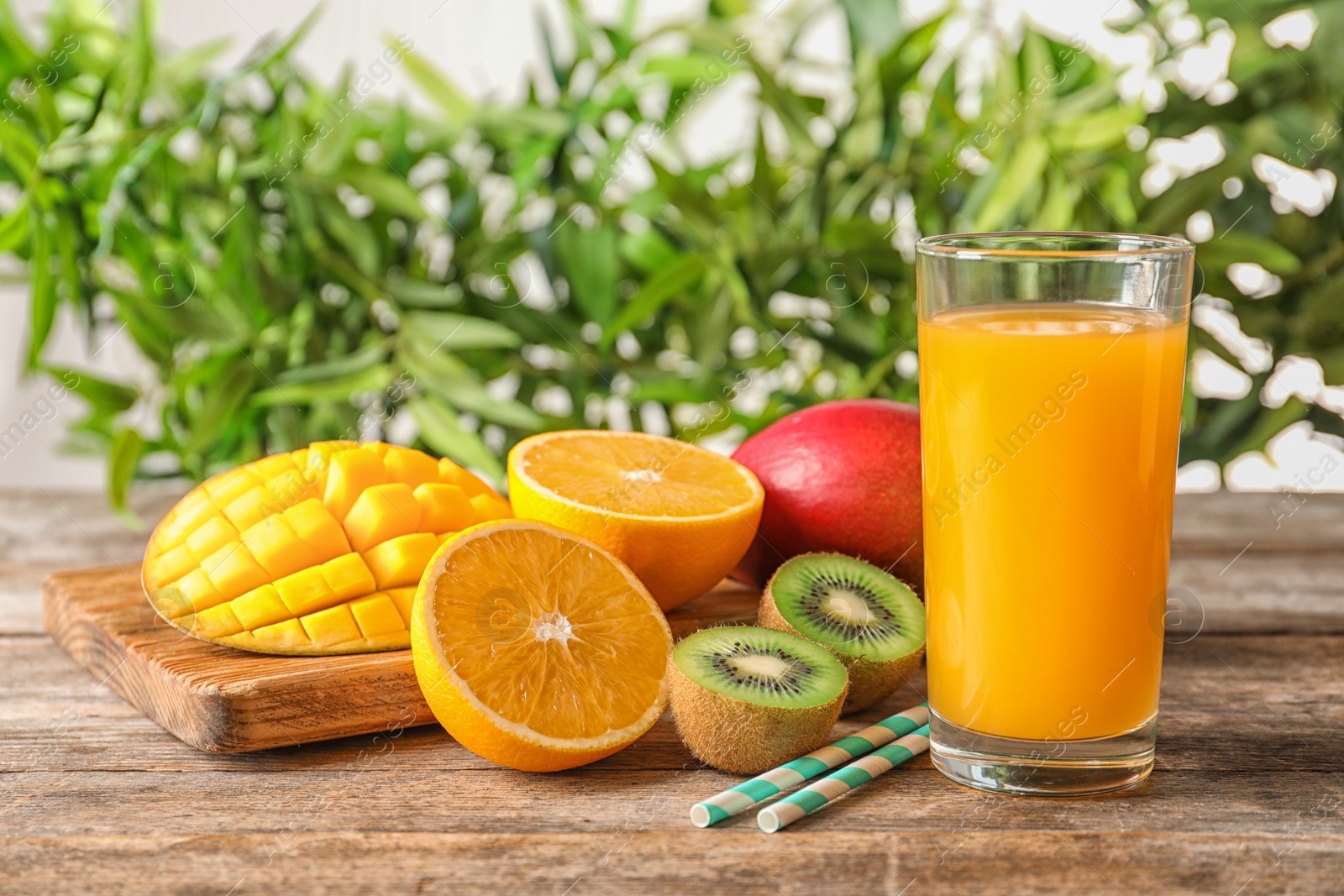 Photo of Tasty tropical drink with mango and fresh fruits on wooden table against blurred background