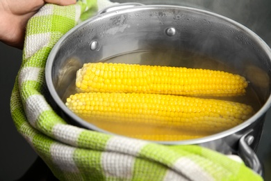 Photo of Person holding pot with boiled corns in hot water on stove, closeup
