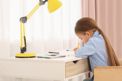 Photo of Cute little girl drawing with marker at desk in room. Home workplace