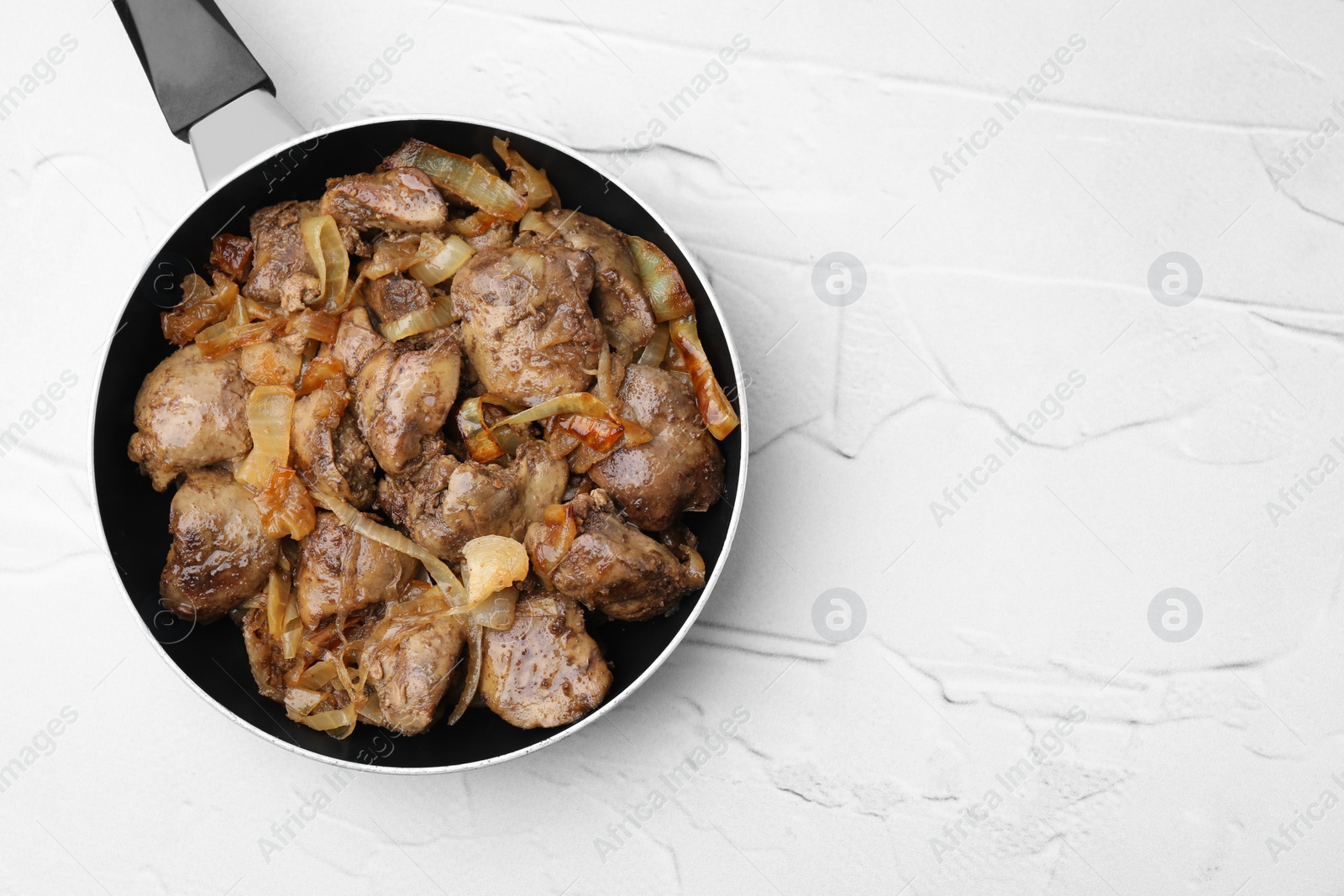 Photo of Pan with tasty fried chicken liver and onion on white textured table, top view. Space for text