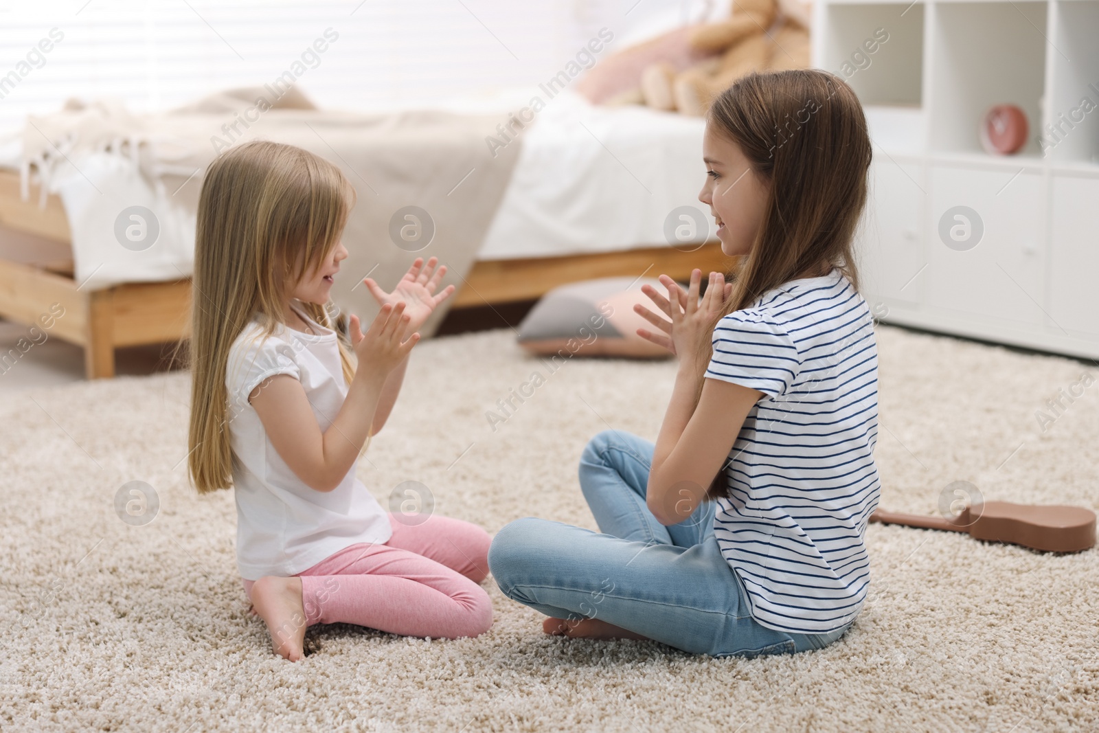 Photo of Cute little sisters playing clapping game with hands at home