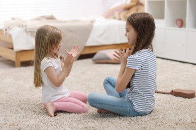 Cute little sisters playing clapping game with hands at home
