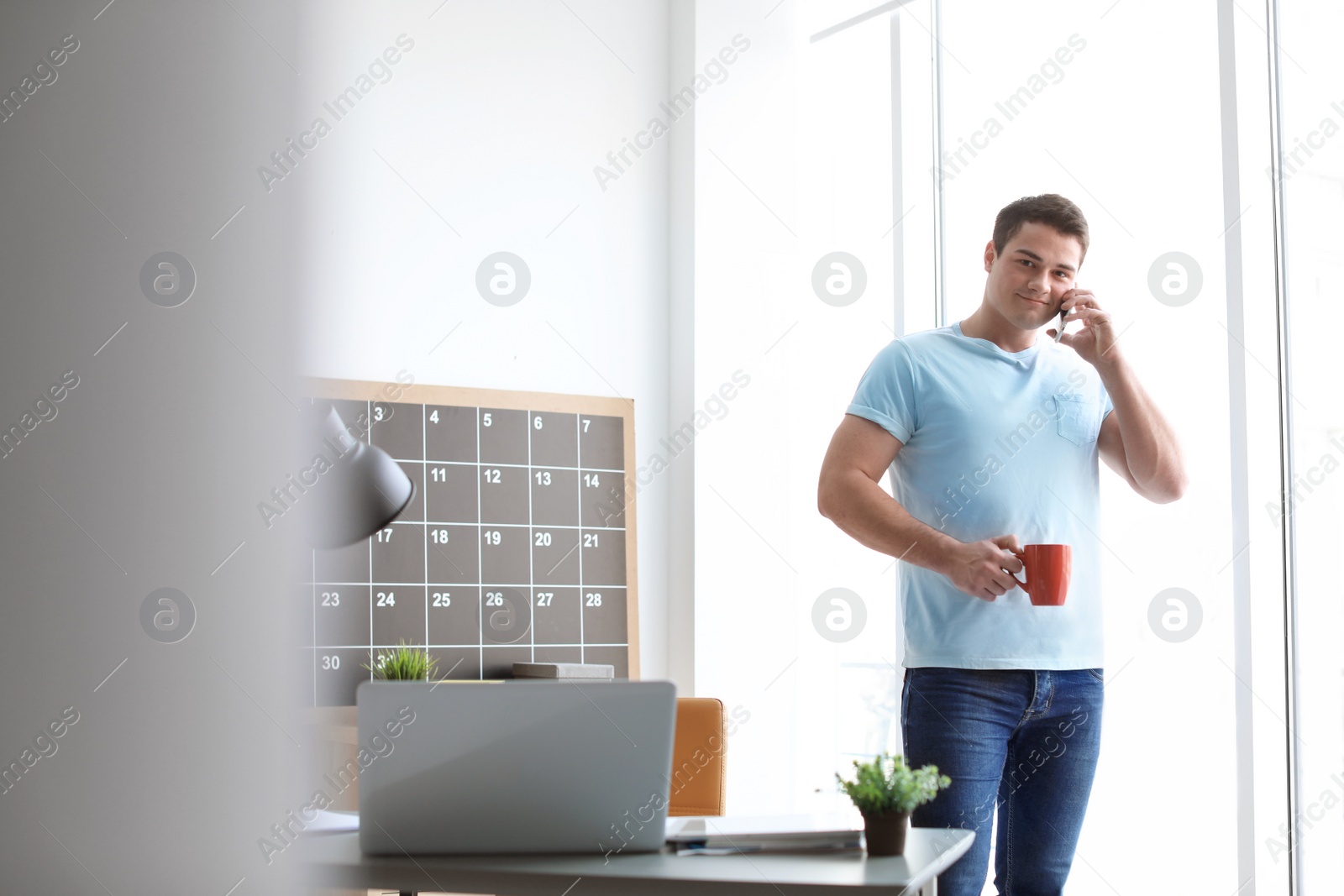 Photo of Portrait of confident young man talking on mobile phone near table in room