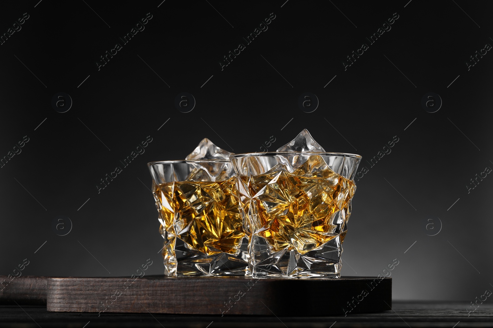 Photo of Whiskey and ice cubes in glasses on black wooden table, closeup