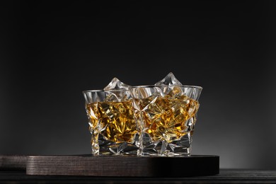 Photo of Whiskey and ice cubes in glasses on black wooden table, closeup