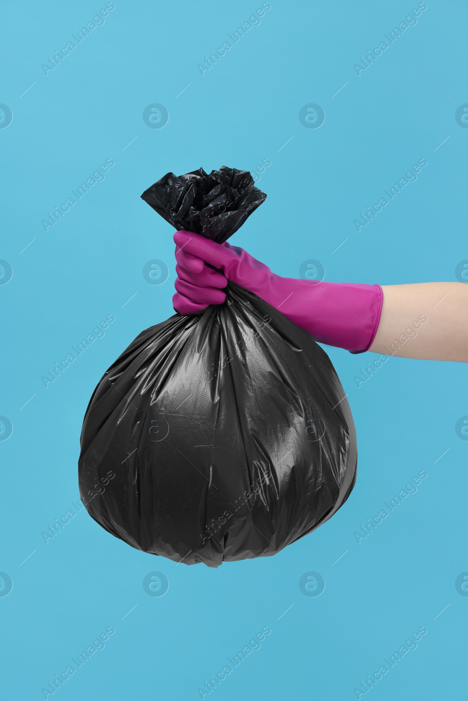 Photo of Woman holding plastic bag full of garbage on light blue background, closeup