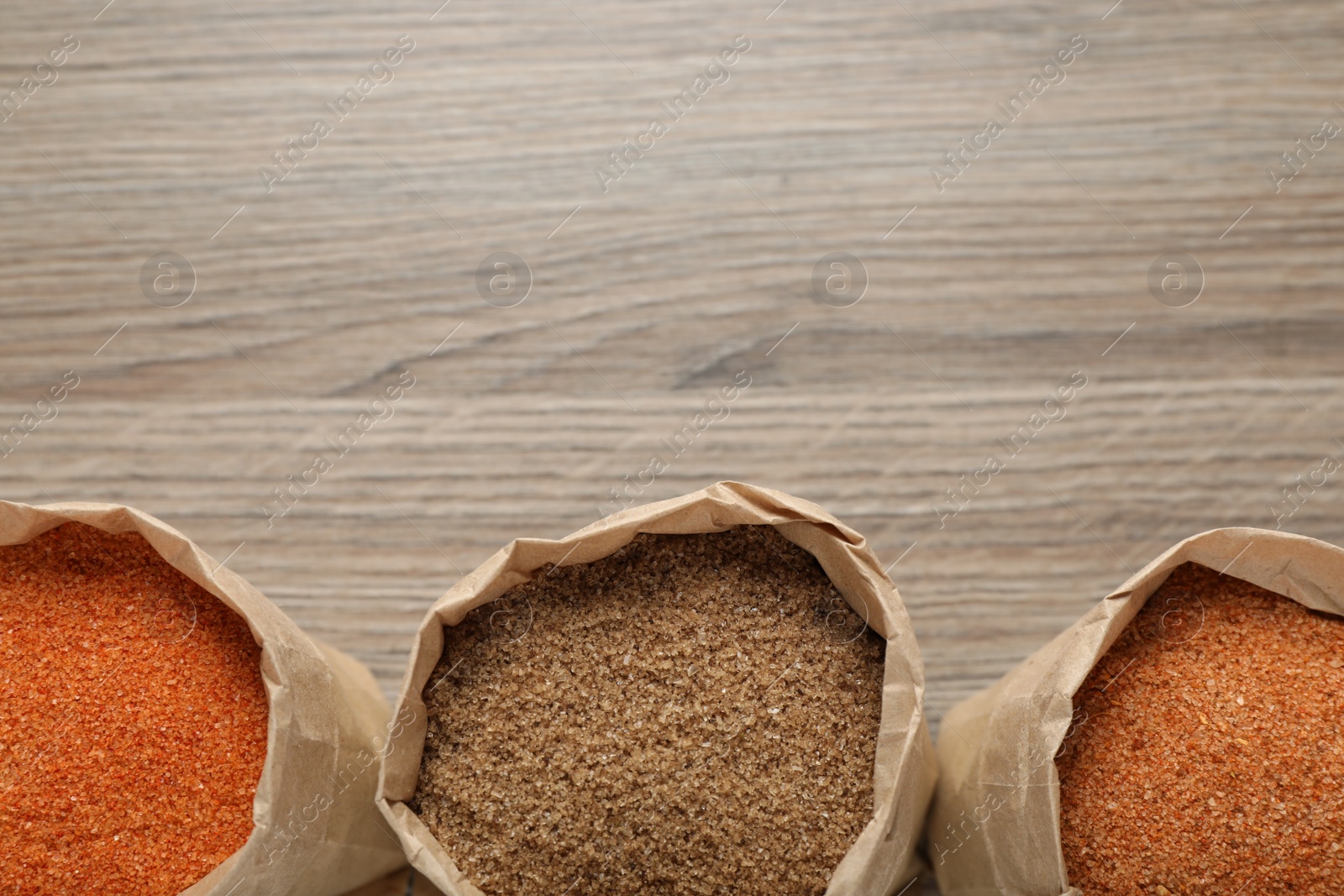 Photo of Different kinds of salt in paper bags on wooden table, flat lay. Space for text