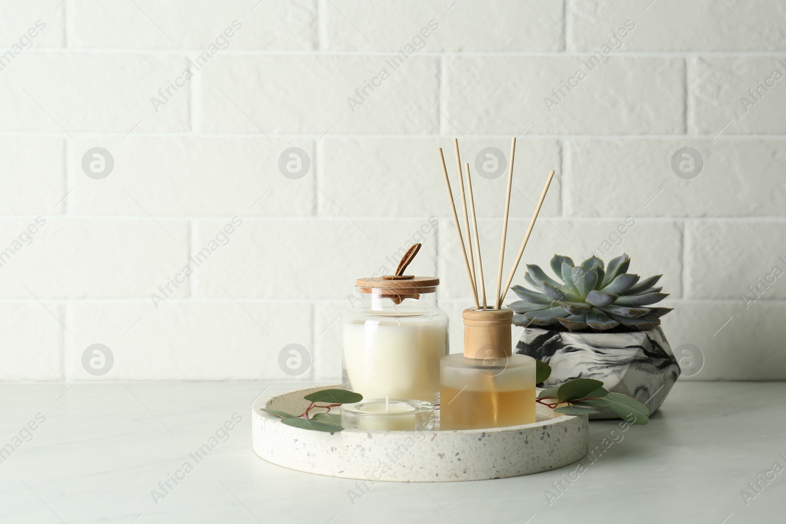 Photo of Candles, eucalyptus branches and aromatic reed air freshener on white table near brick wall, space for text. Interior elements