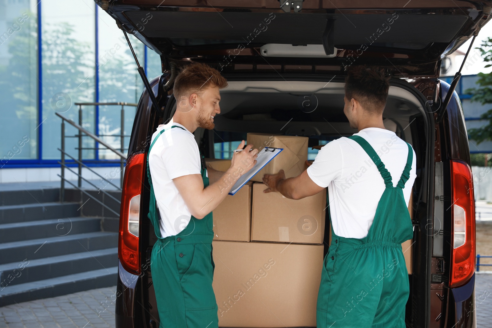 Photo of Young couriers near delivery car with many parcels outdoors