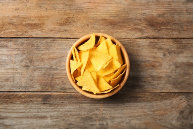 Photo of Tasty mexican nachos chips in bowl on wooden table, top view