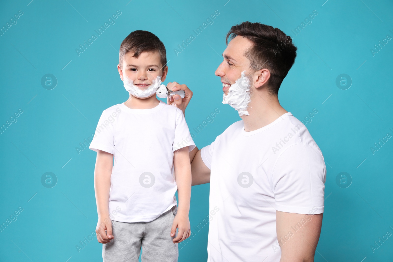 Photo of Dad applying shaving foam onto son's face against color background