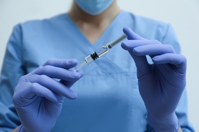 Doctor holding syringe with COVID-19 vaccine on light background, closeup