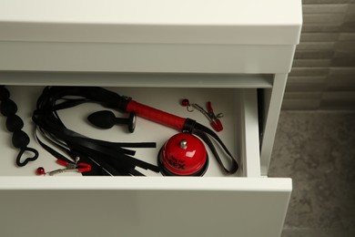 Photo of Whip, nipple clamps, bell and anal plug in drawer indoors. Sex toys