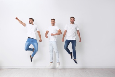 Group of young men in jeans jumping near light wall