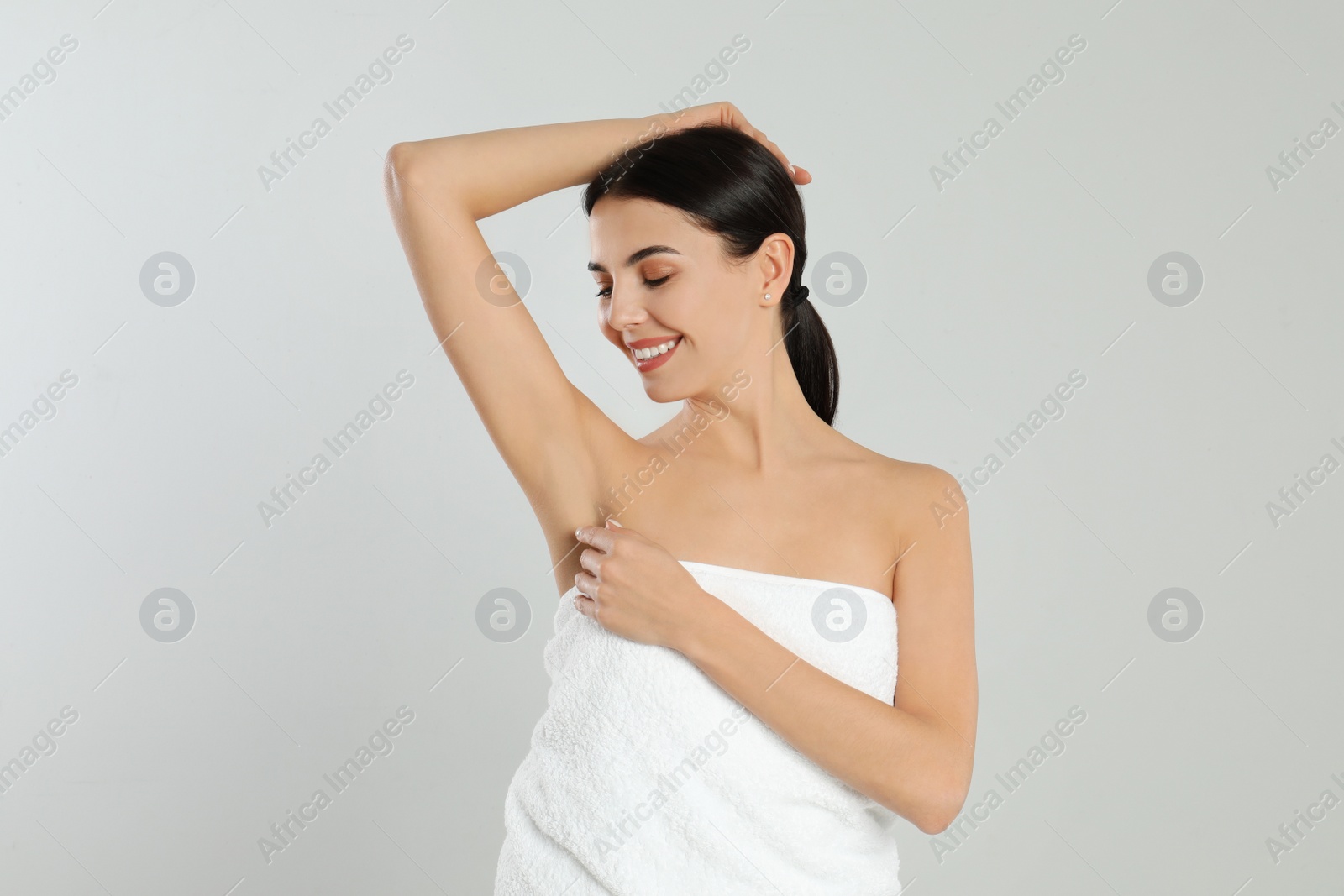 Photo of Young woman showing hairless armpit after epilation procedure on light grey background