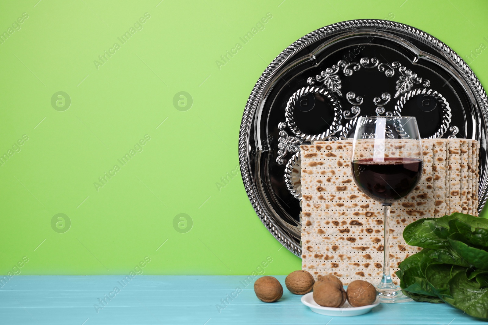 Photo of Symbolic Pesach (Passover Seder) items on wooden table against green background, space for text