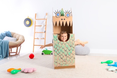 Photo of Cute little boy playing with cardboard dragon at home
