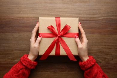 Photo of Woman holding Christmas gift box at wooden table, top view