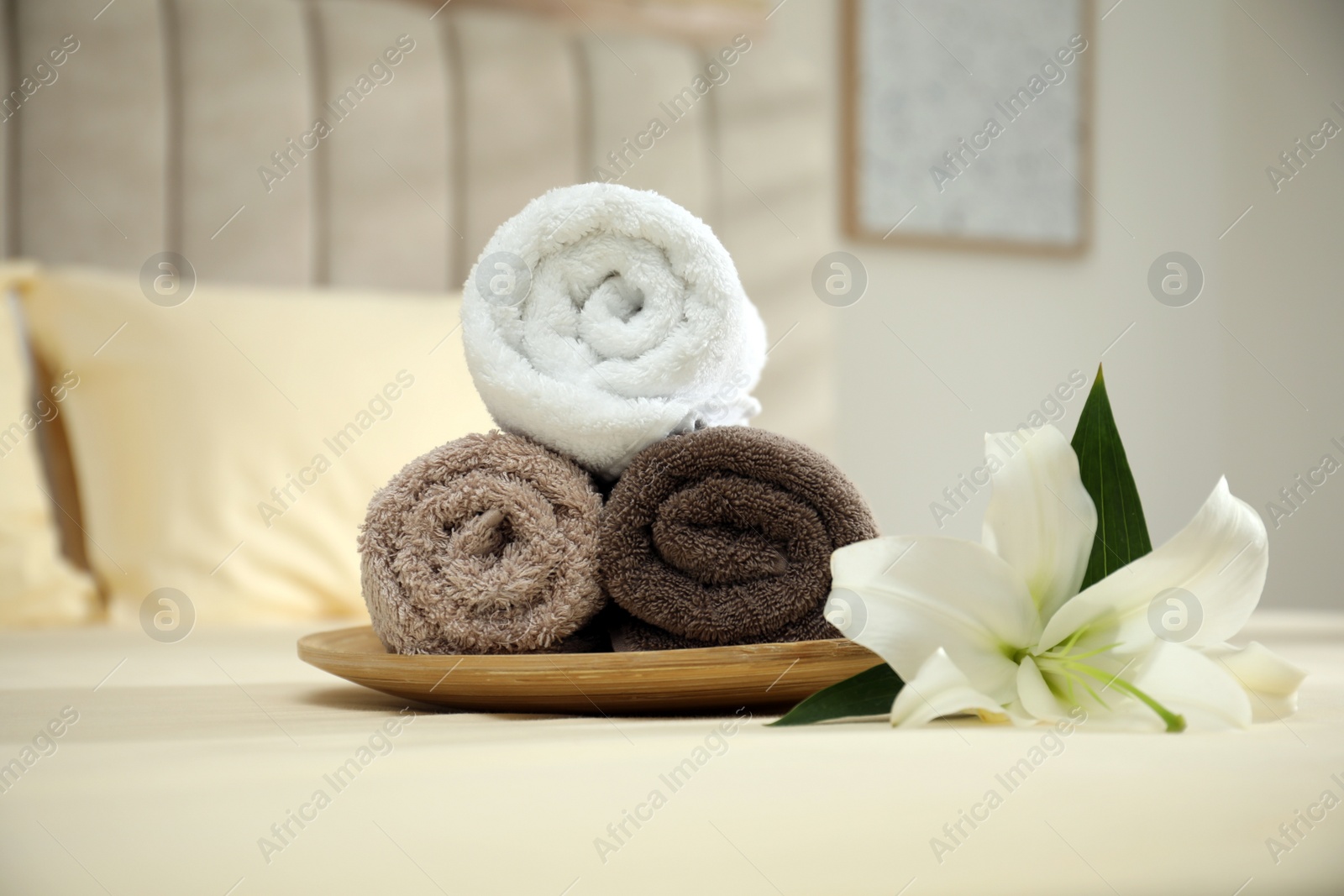 Photo of Rolled clean towels and flower on bed indoors