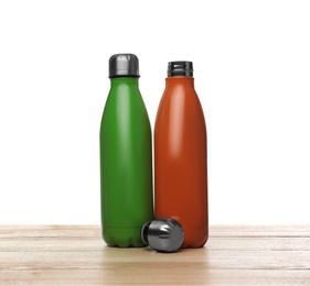 Photo of Stylish thermo bottles on wooden table against white background