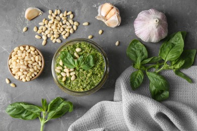 Photo of Jar of delicious pesto sauce and ingredients on grey table, flat lay