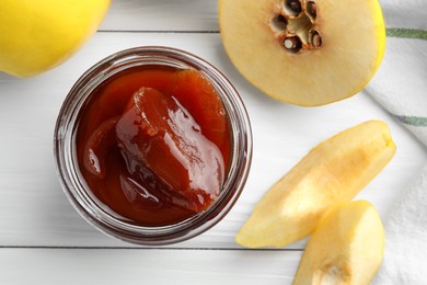 Photo of Tasty homemade quince jam in jar and fruits on white wooden table, flat lay