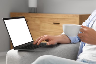 Man with cup of drink using laptop at home, closeup
