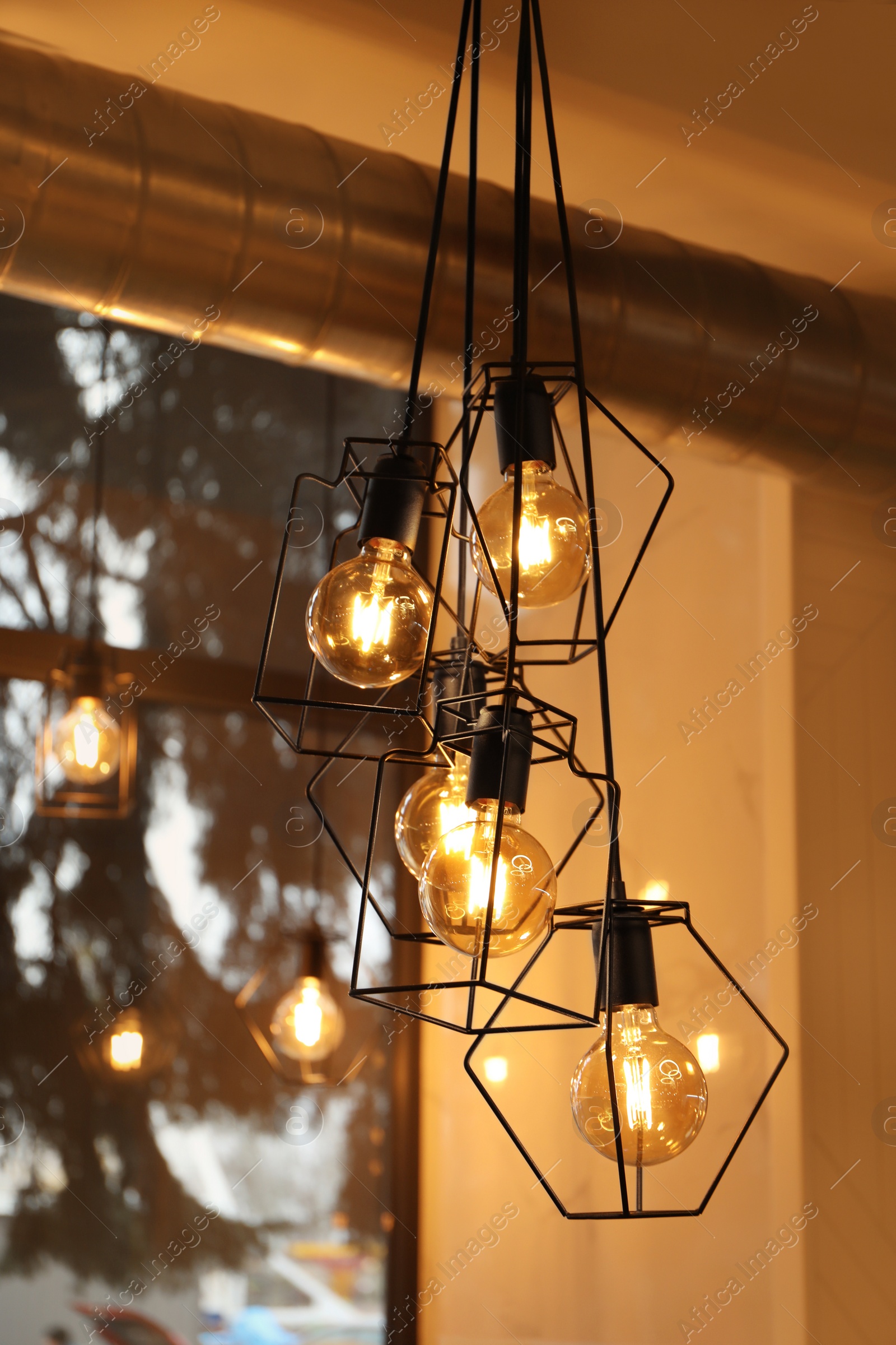 Photo of Pendant lamps with glowing light bulbs near window indoors