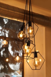 Photo of Pendant lamps with glowing light bulbs near window indoors