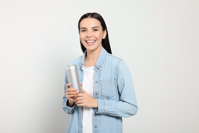 Beautiful happy woman holding beverage can on light grey background