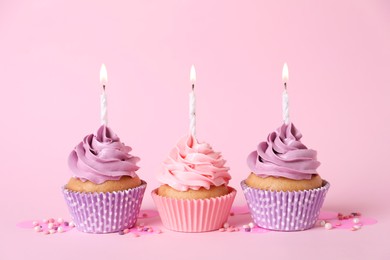 Delicious birthday cupcakes with burning candles and sprinkles on pink background