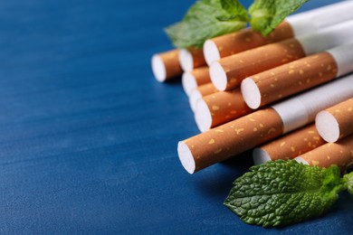 Photo of Menthol cigarettes and mint leaves on blue wooden table, closeup. Space for text
