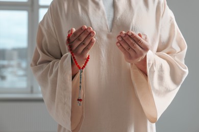 Photo of Muslim man with misbaha praying indoors, closeup