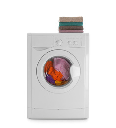 Modern washing machine with laundry and stack of towels on white background