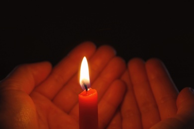 Photo of Young person holding burning candle in darkness, closeup