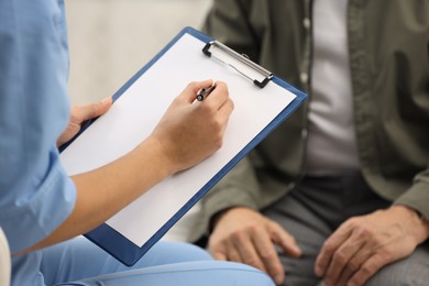 Photo of Nurse with clipboard and elderly patient indoors, closeup