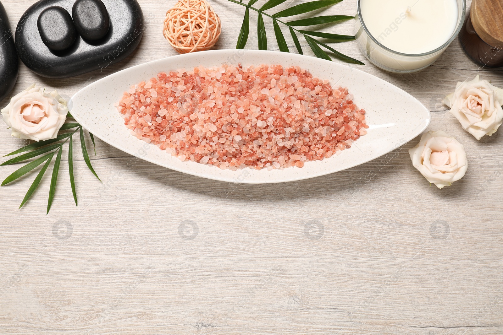 Photo of Natural sea salt, spa stones, candle and floral decor on wooden table, flat lay. Space for text