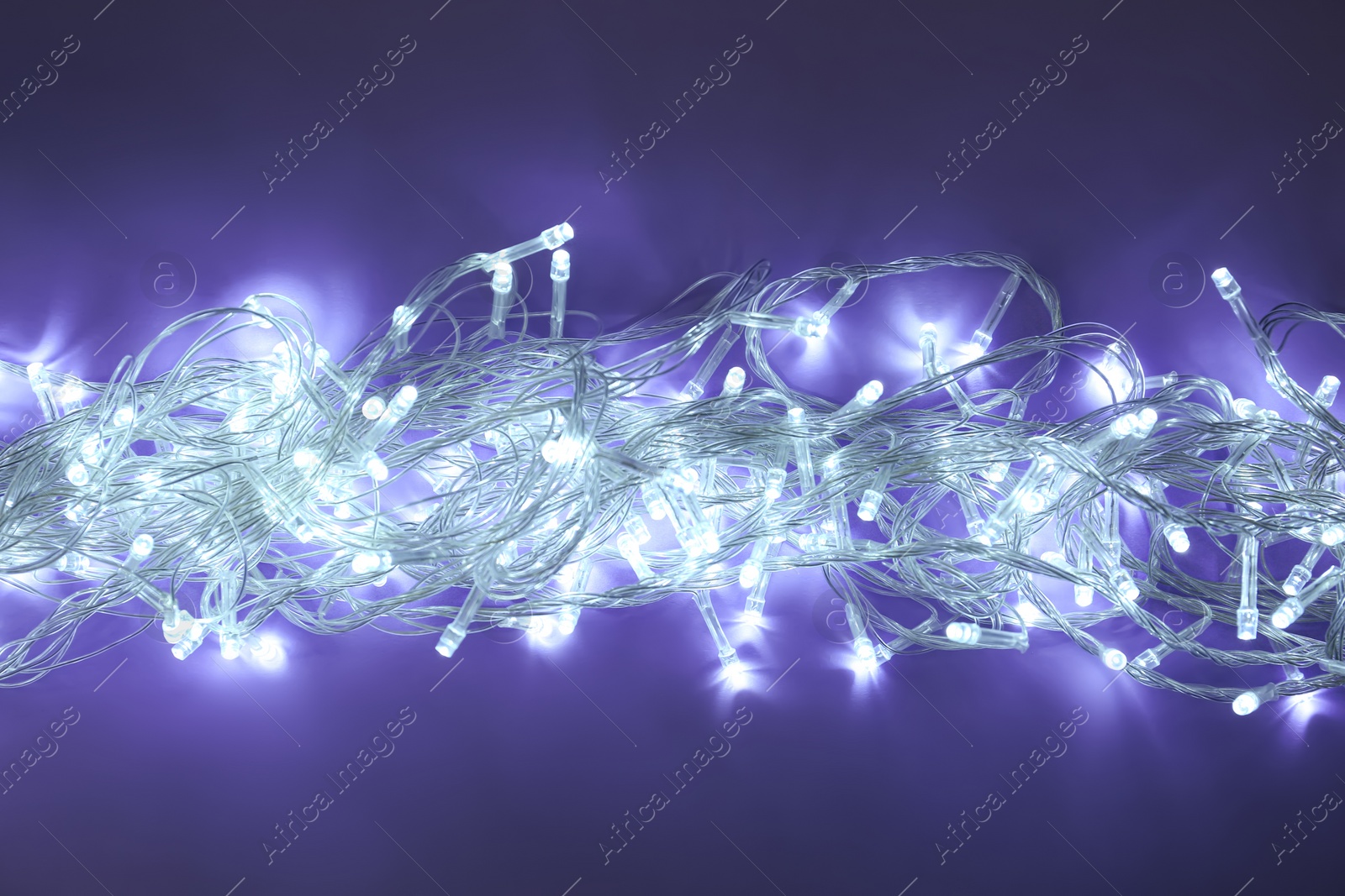 Photo of Glowing Christmas lights on dark violet background, top view