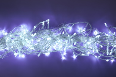 Photo of Glowing Christmas lights on dark violet background, top view