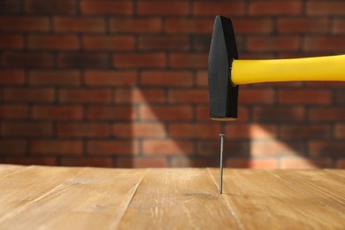 Photo of Hammering metal nail on wooden table against brick wall. Space for text